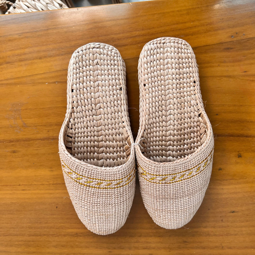 Top view of beige woven straw slippers with yellow decorative trim, placed on a wooden surface. Features breathable natural fiber texture, lightweight soft sole, ideal for summer beach wear or casual indoor use.
