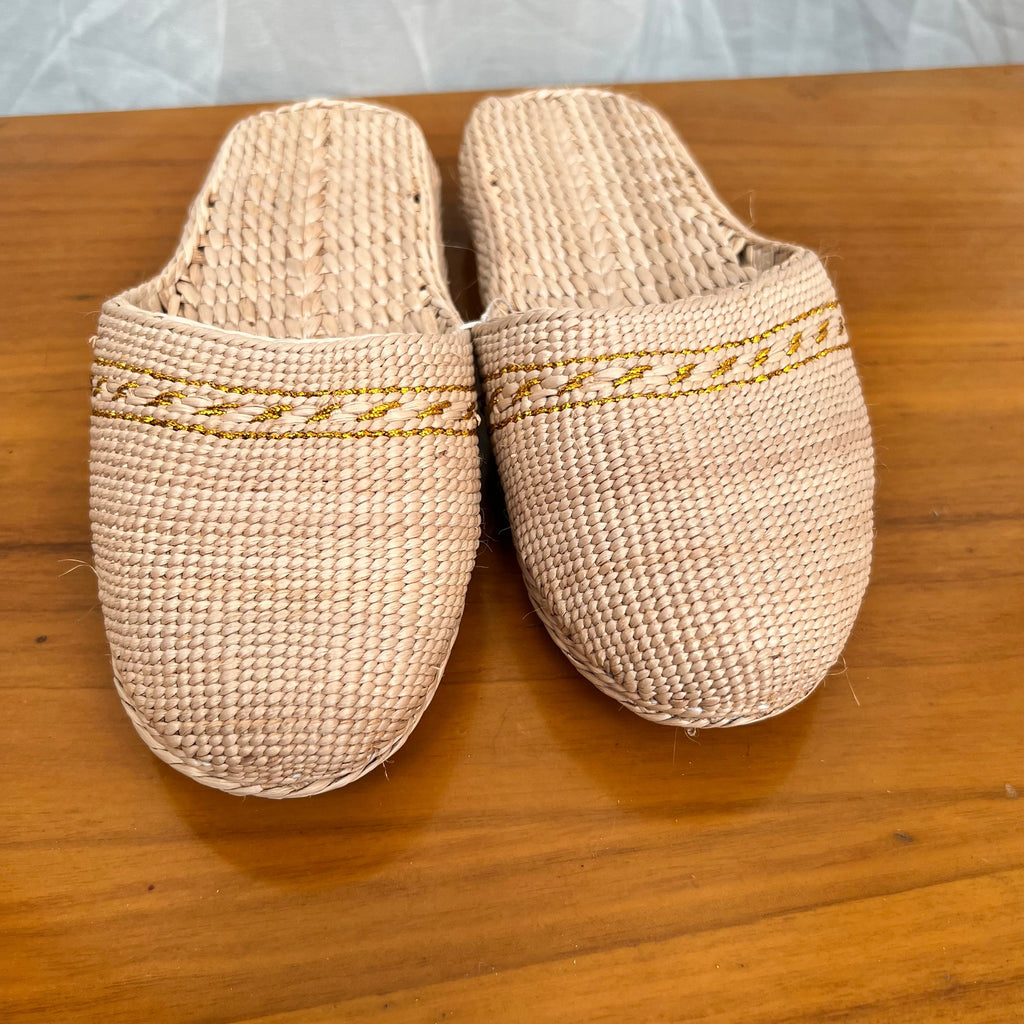 Front view of beige woven straw slippers with yellow decorative trim, placed on a wooden surface. Features soft sole, breathable texture, and lightweight design for comfortable summer beach or indoor wear.