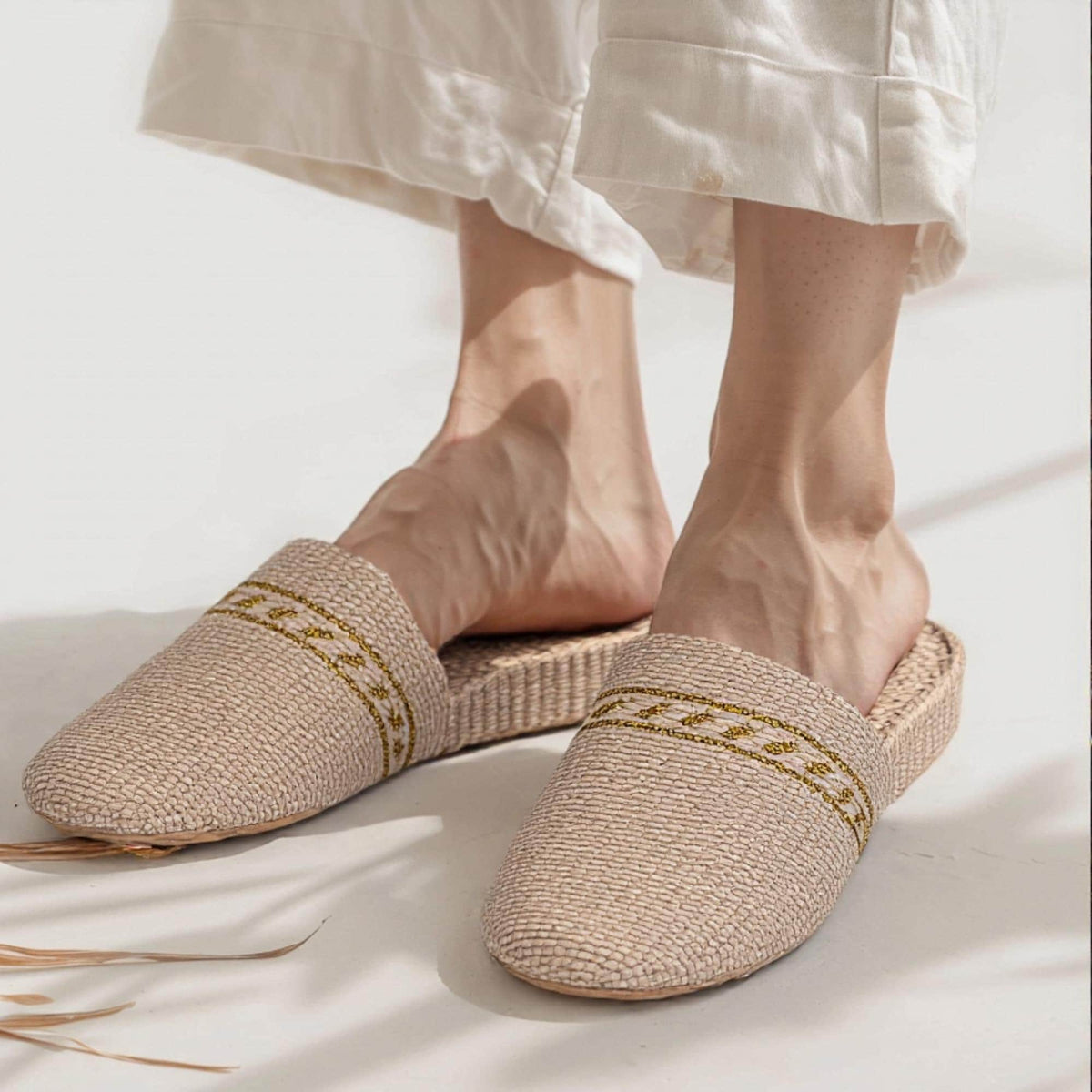 Woman wearing beige woven straw slippers with soft sole and yellow decorative trim. Lightweight, breathable design ideal for summer beach wear, casual slides, and comfortable indoor or outdoor use.