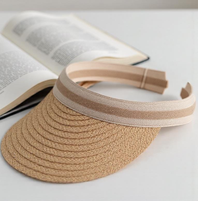 Straw sun hat visor with wide brim rests beside an open book. Lightweight and stylish summer cap for beach, outdoor UV protection, vacation, honeymoon, garden, or a thoughtful gift for her mom.