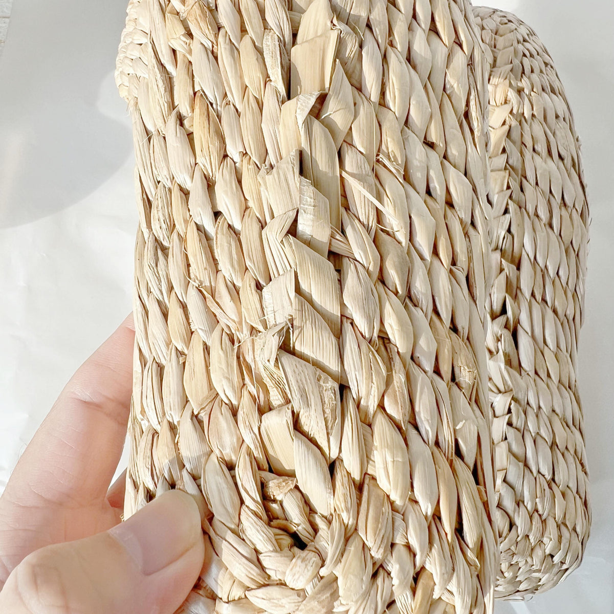 Close-up of the sole of a handmade straw slipper, highlighting the detailed woven pattern and natural beige texture. Held in hand, lightweight and breathable for house shoes.