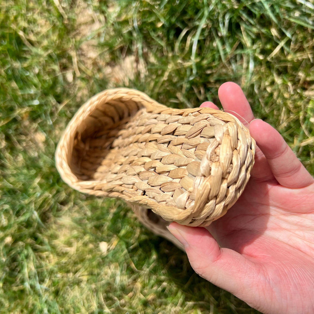 Hand holding a handmade straw slipper outdoors on grass, showing woven texture and thick sole. Natural beige color, lightweight and breathable, perfect for summer house shoes.