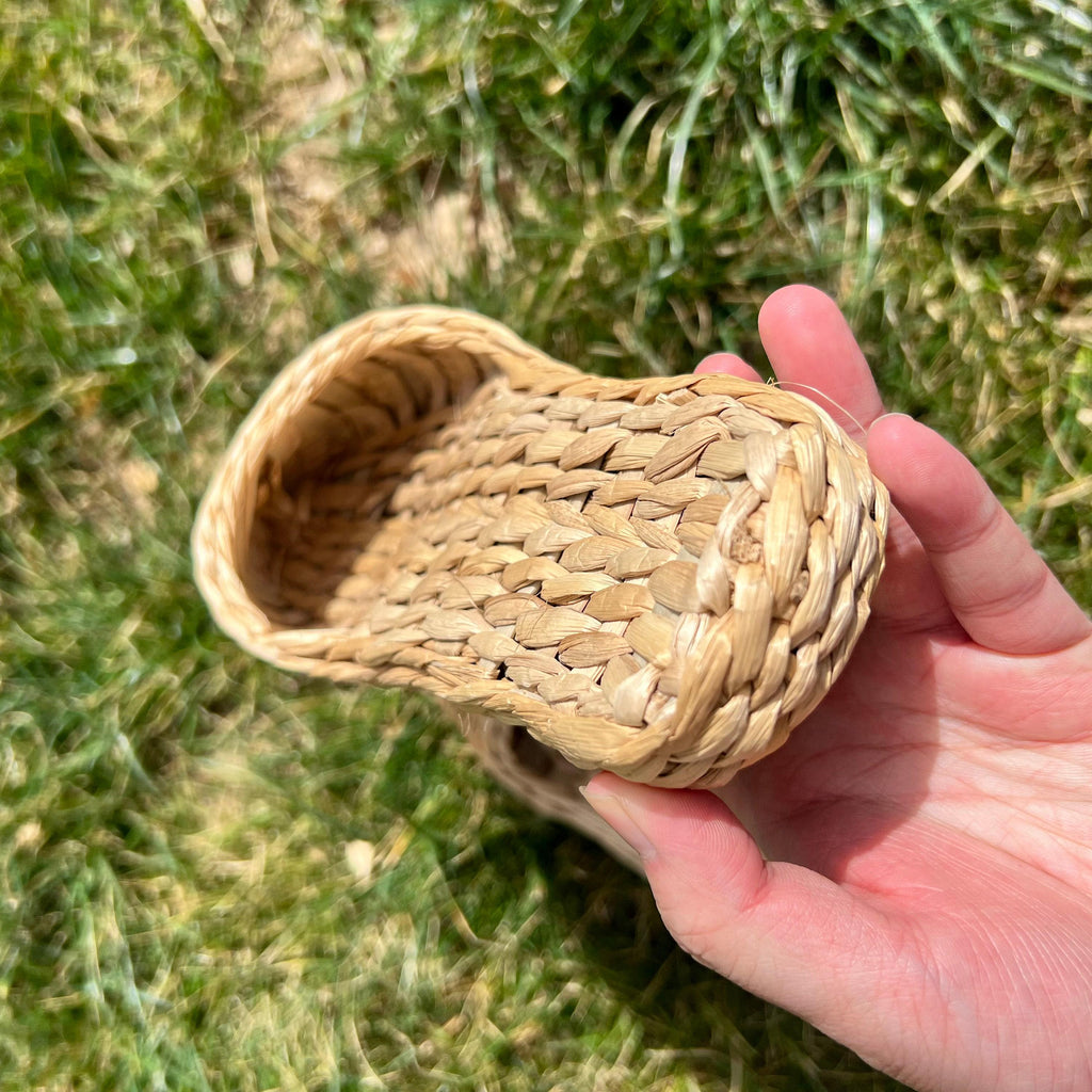Hand holding a handmade straw slipper outdoors on grass, showing closed toe design, woven texture, and thick sole. Natural beige color, lightweight and breathable for summer wear.