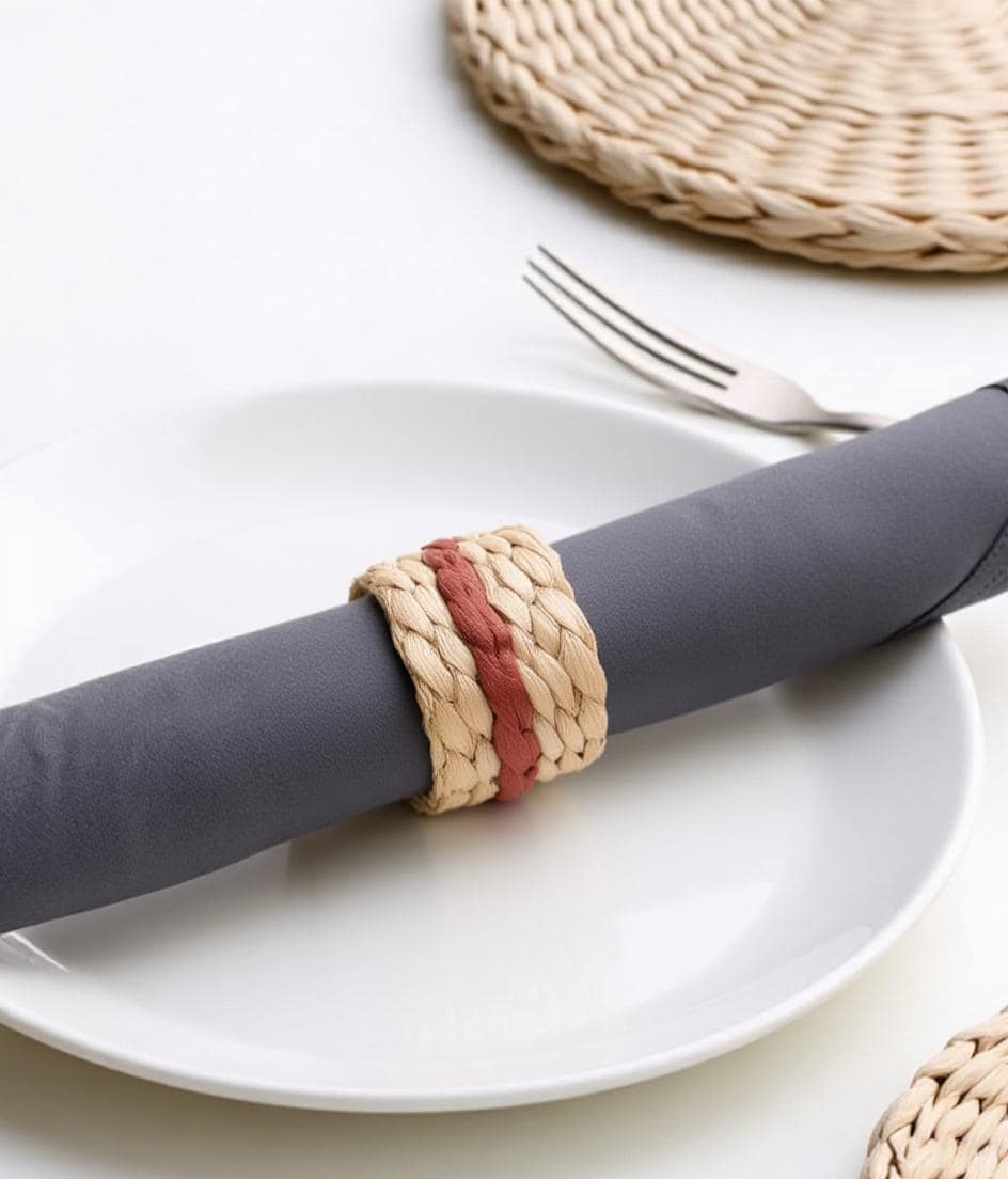 A white plate with a gray napkin rolled up in a napkin ring, accompanied by a fork and a woven placemat.