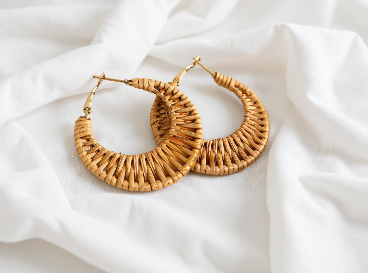 A pair of gold earrings made of woven material, placed on a white fabric background.