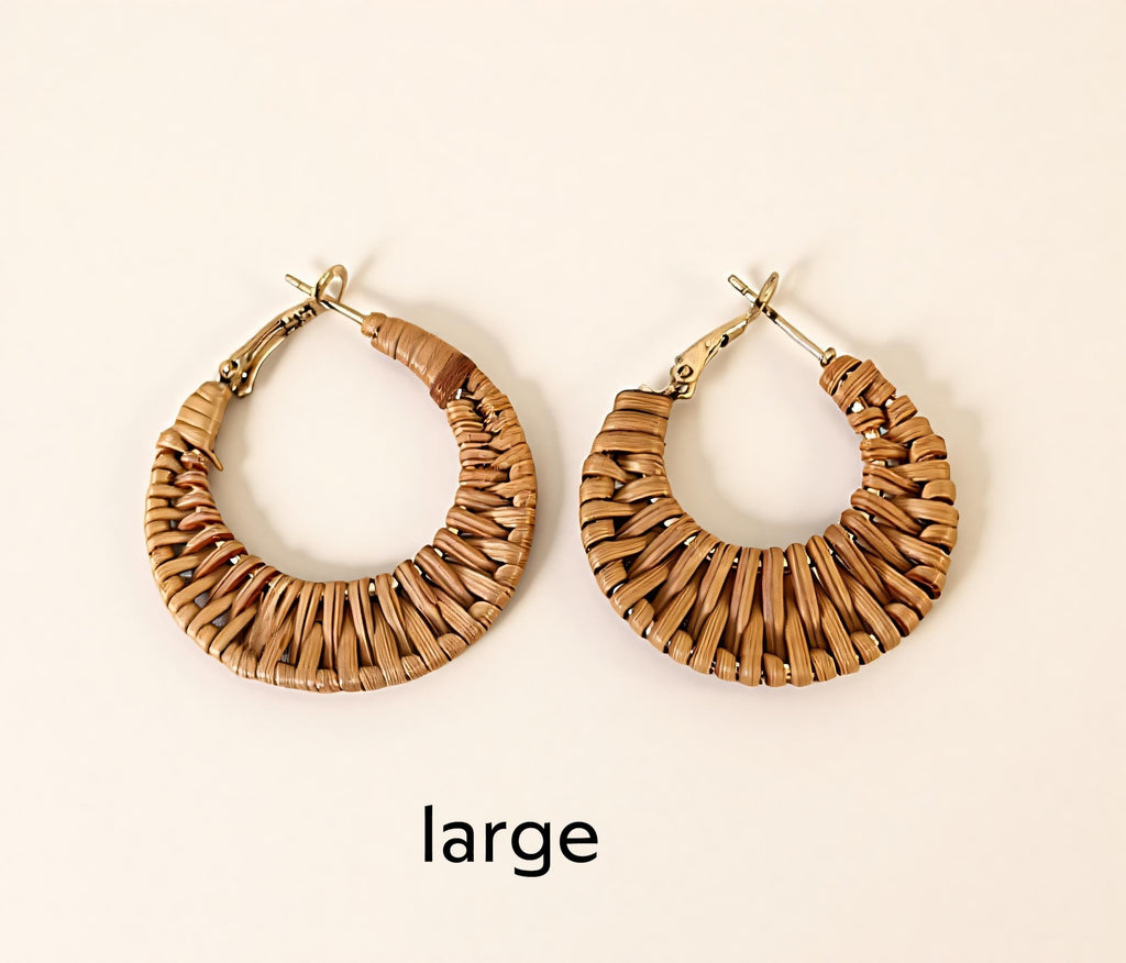 Two large earrings made of woven material, possibly straw or reed, are displayed against a white background.