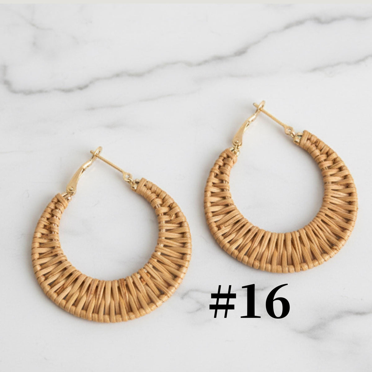 A pair of gold hoop earrings made of woven material, placed on a marble surface.