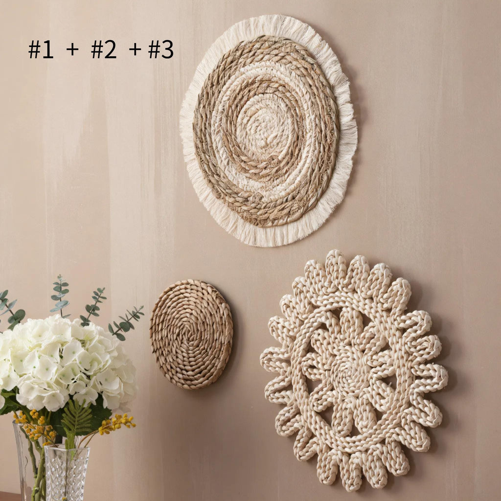 a beige wall with three decorative items hanging on it: a round woven mat, a round woven mat with frills, and a round woven mat with a flower design. In addition to these items, there is a vase filled with white flowers placed on the left side of the wall.