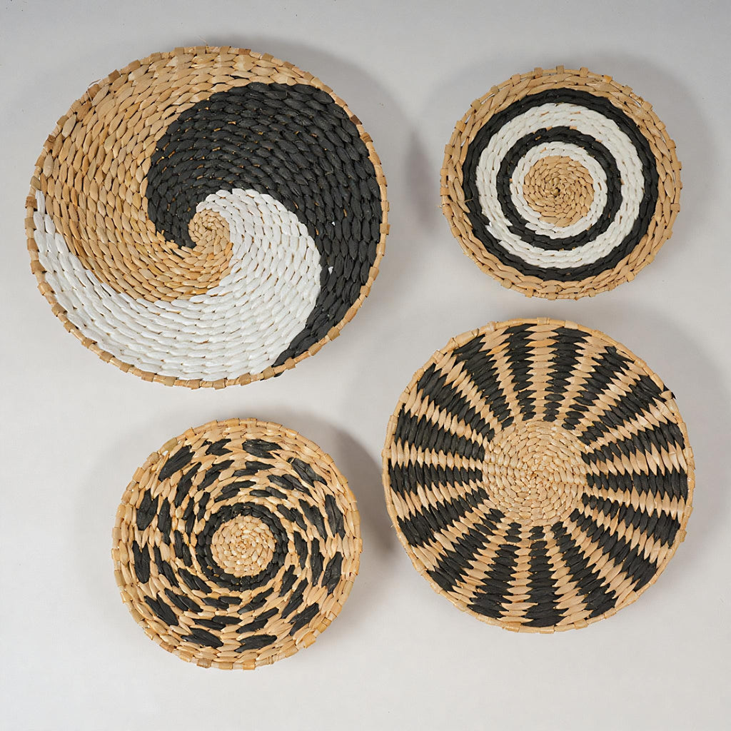 four woven baskets with distinct patterns and colors, including a large circular basket with a black and white spiral pattern, a smaller circular basket with a black and white striped pattern, and two smaller circular baskets with a black and white striped pattern.