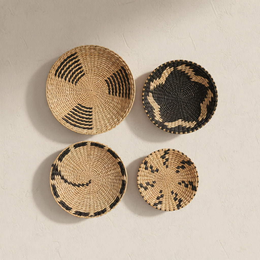 four woven baskets of different sizes and shapes, arranged on a white wall.
