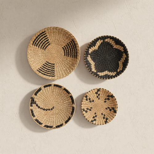 four woven baskets of different sizes and shapes, arranged on a white wall.