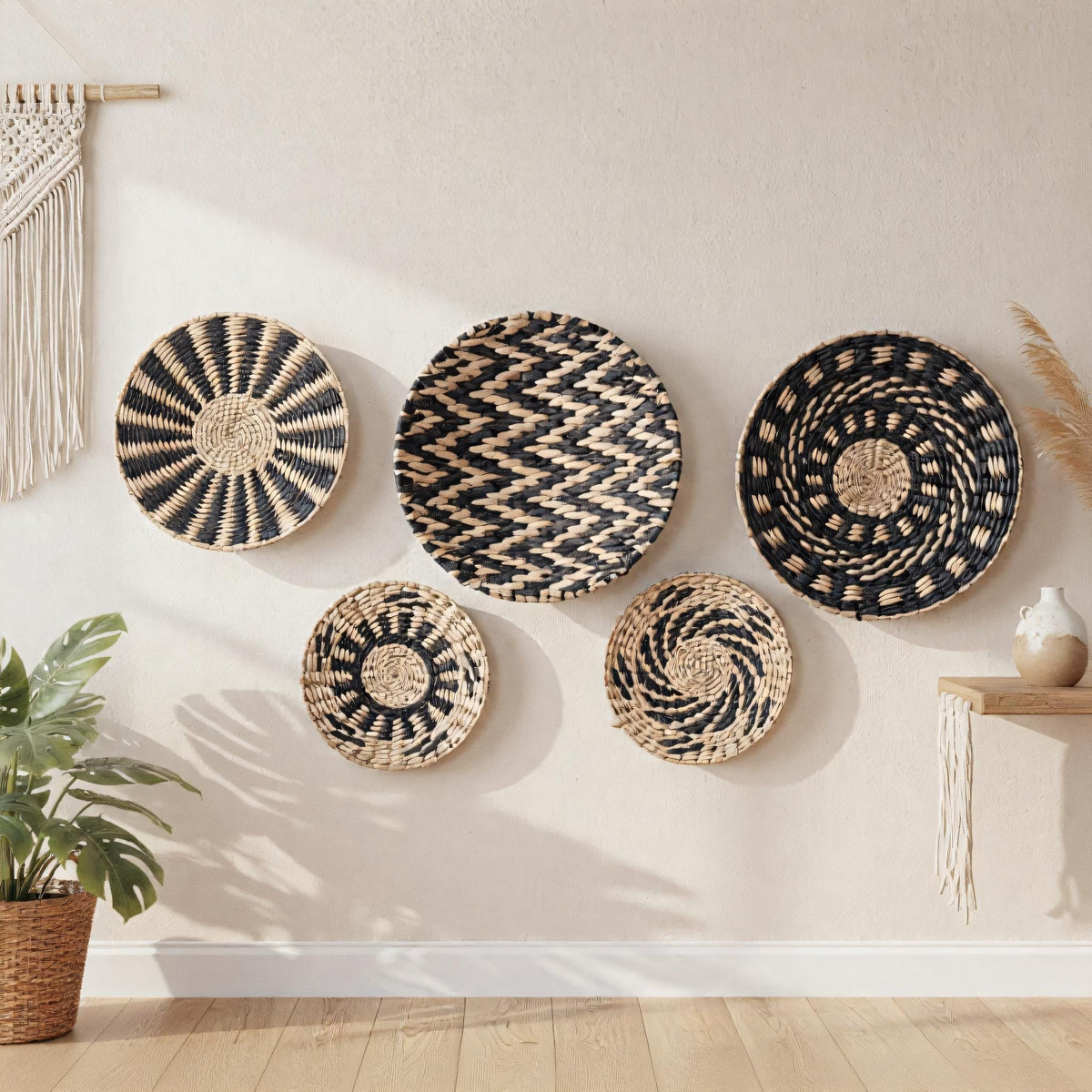 a wall adorned with five woven baskets in various patterns, including a zigzag pattern, a circular pattern, and a spiral pattern. The baskets are hanging on the wall, creating a visually appealing display. In addition to the baskets, there is a potted plant and a vase on a shelf, adding to the overall aesthetic of the room.