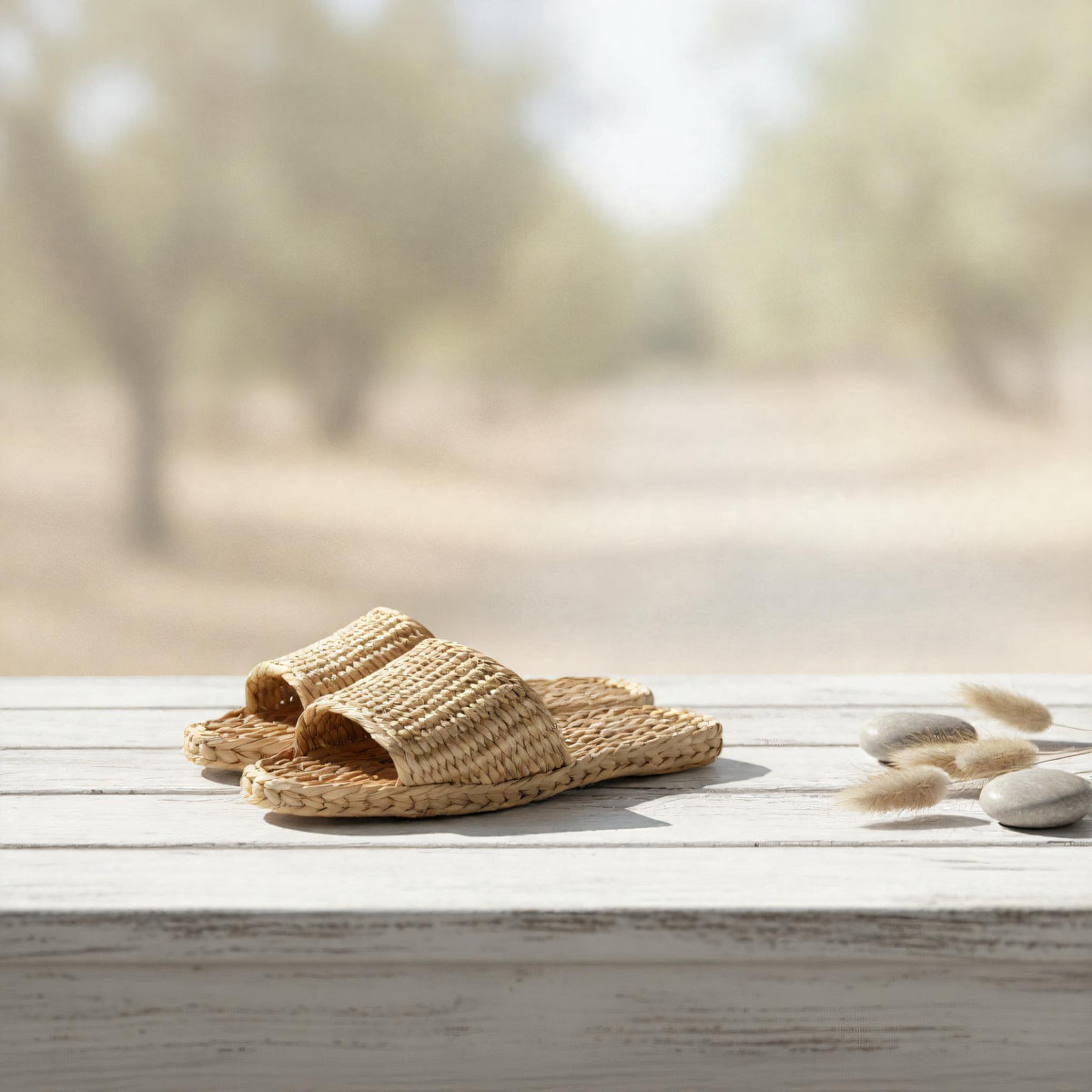 A pair of woven sandals sits on a wooden surface, with a blurred natural background suggesting a serene outdoor setting.