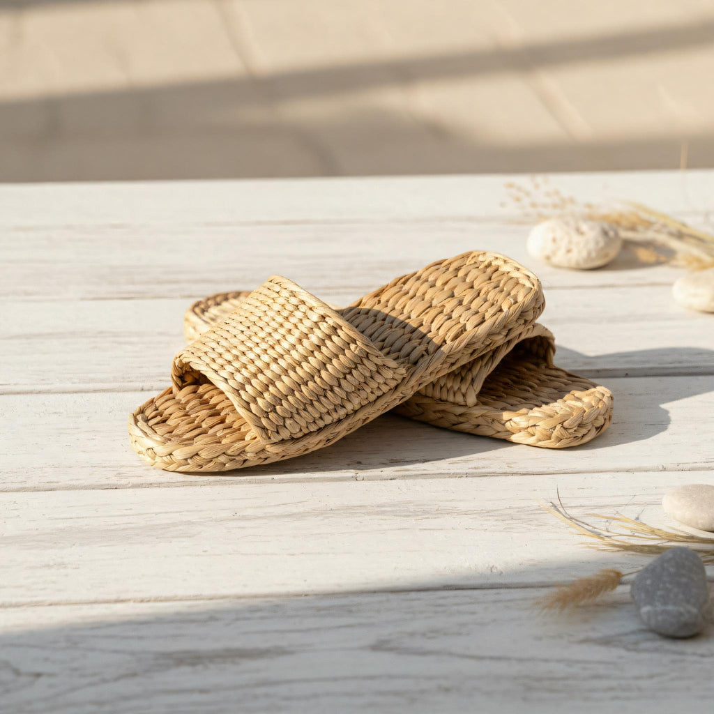 A pair of woven sandals sits on a wooden surface, with some rocks and dried plants nearby.