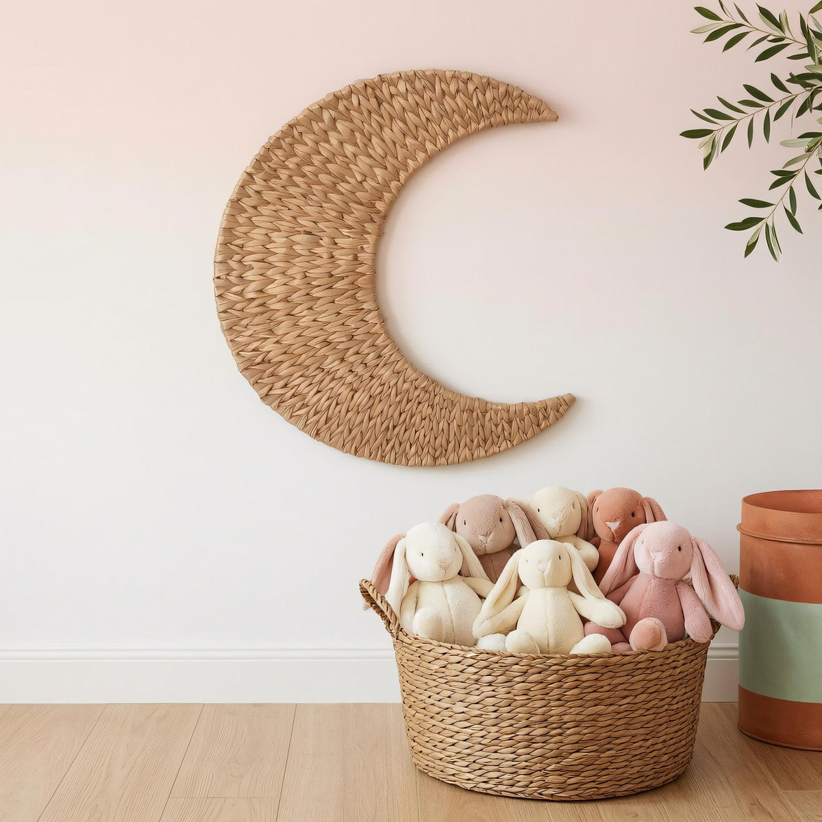 A woven basket filled with stuffed rabbits sits on a wooden floor, with a crescent moon-shaped decoration hanging on the wall above it.