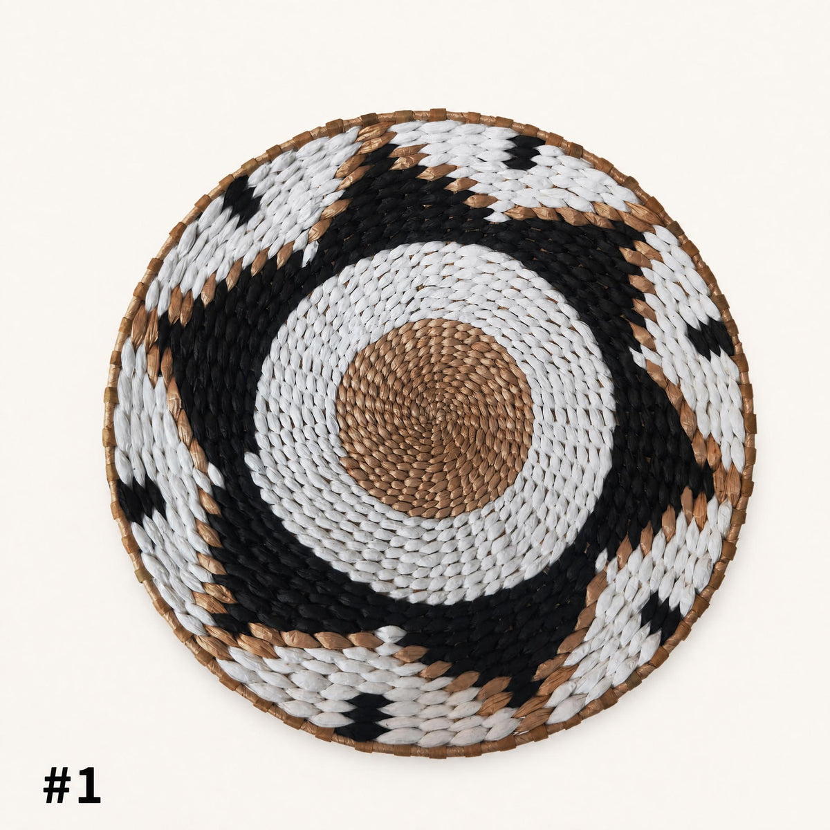 A woven mat with a circular design in black, white, and brown colors.