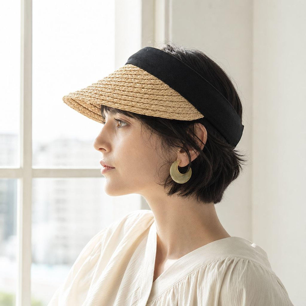 A woman wearing a straw hat and earrings is looking out a window.