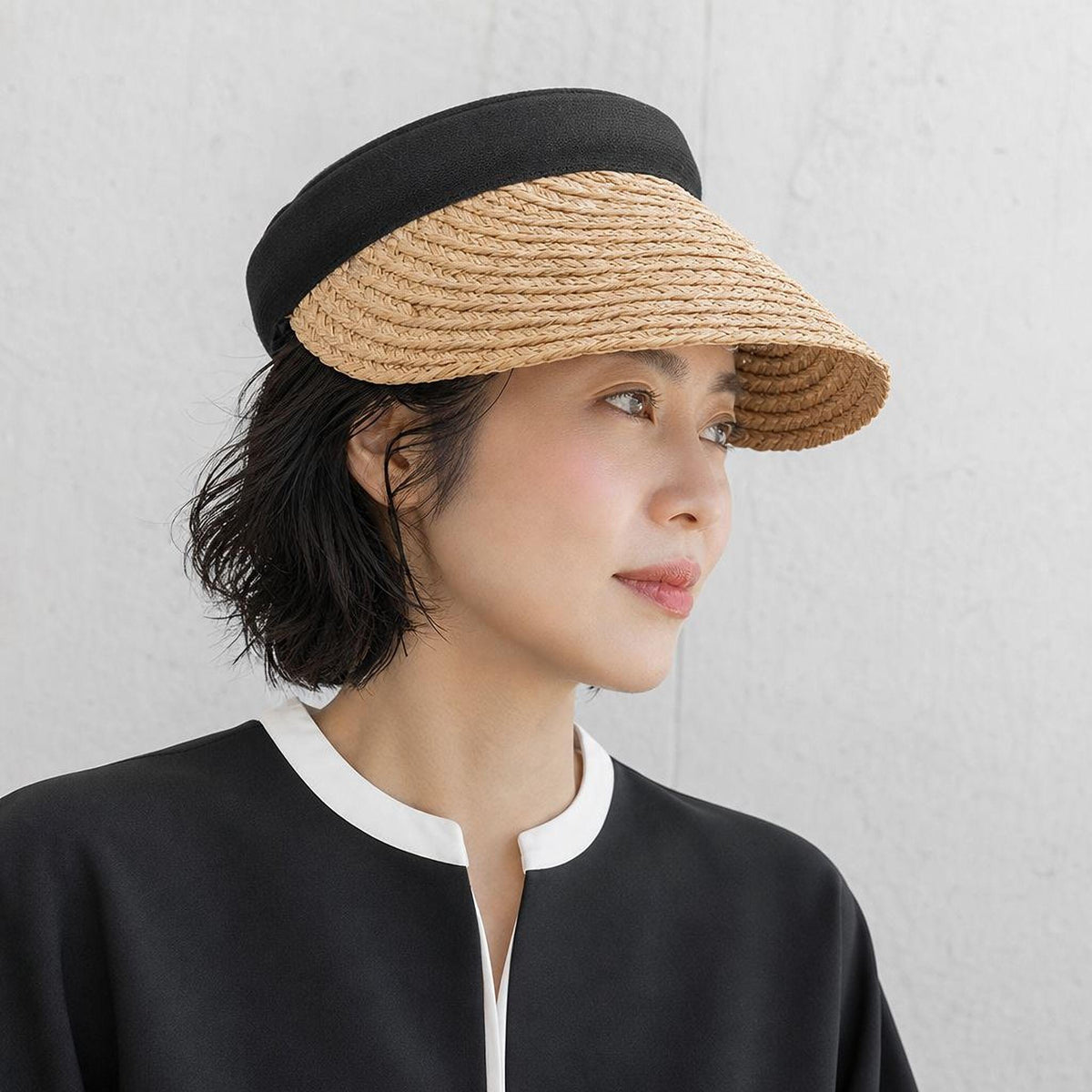 A woman wearing a straw hat and a black top is looking off to the side.