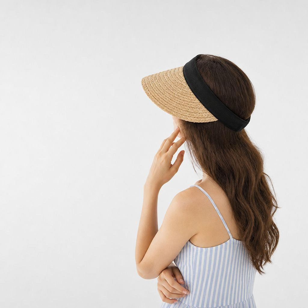 A woman with long brown hair wearing a straw hat and a striped dress stands with her hand on her chin, facing away from the camera.