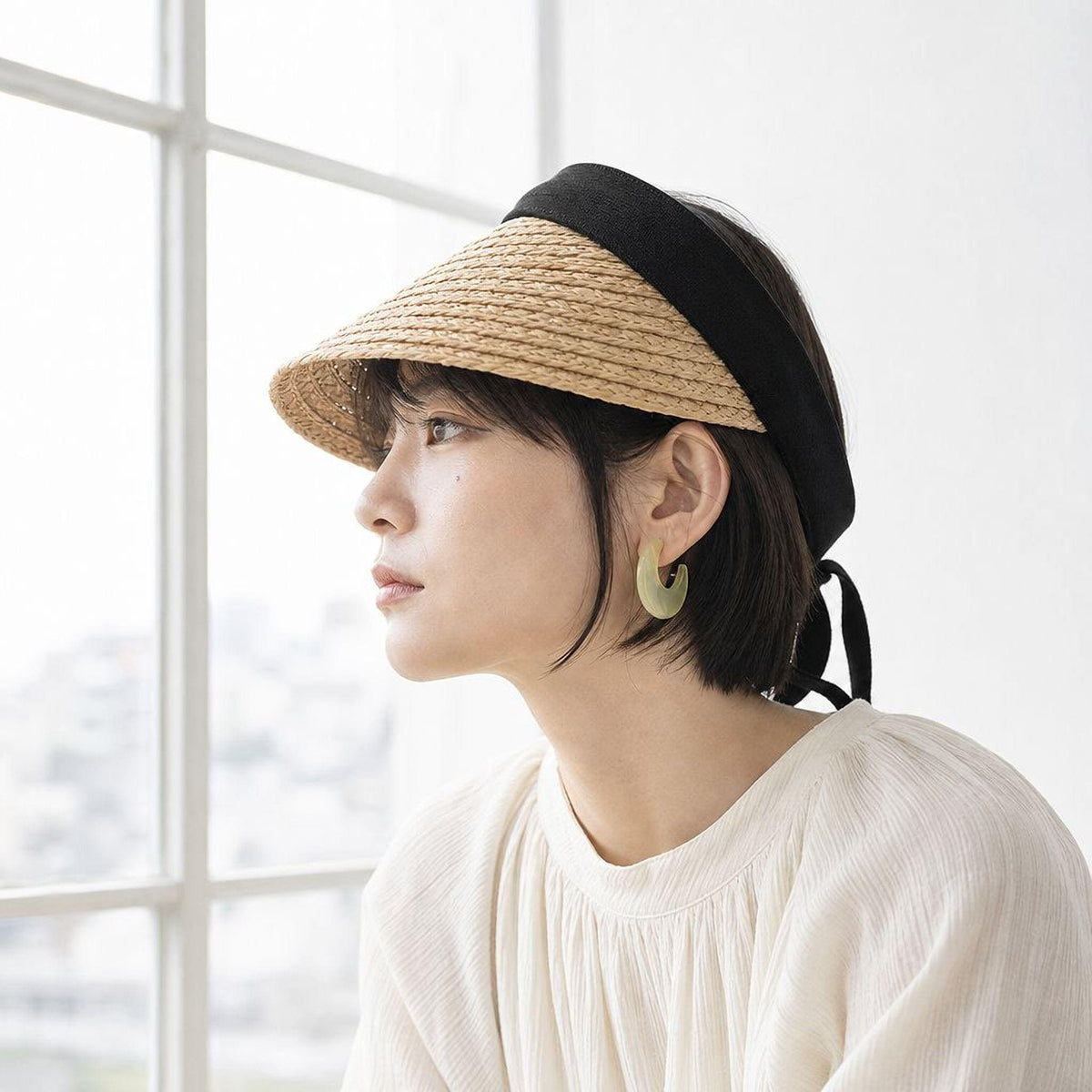 A woman wearing a straw hat and earrings is looking out a window. - view 2
