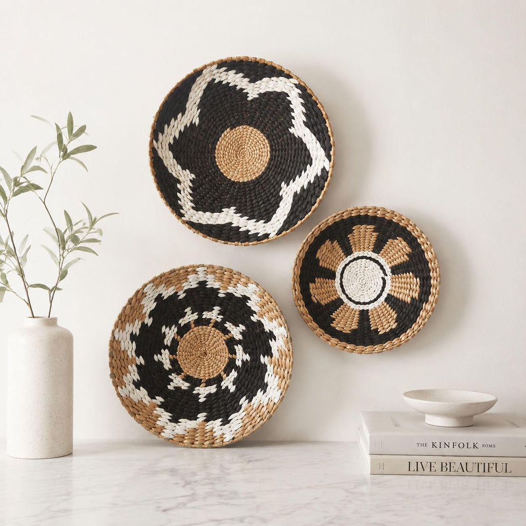 three woven baskets with distinct patterns, including a star-shaped basket, a circular basket with a floral design, and a round basket with a geometric pattern. The baskets are displayed on a white marble countertop, with a small white vase and a stack of books nearby.