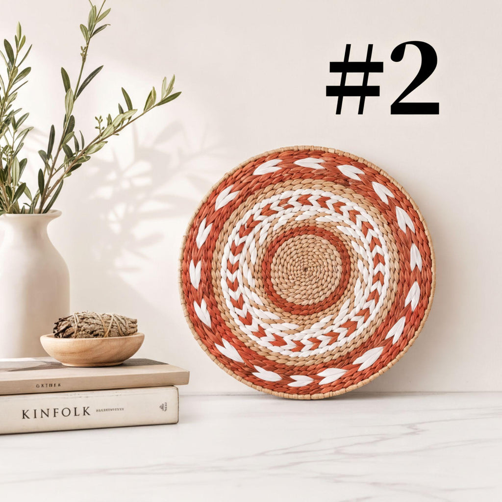 a woven basket with a circular pattern, a stack of books, a white vase with greenery, and a plant on a white marble surface.