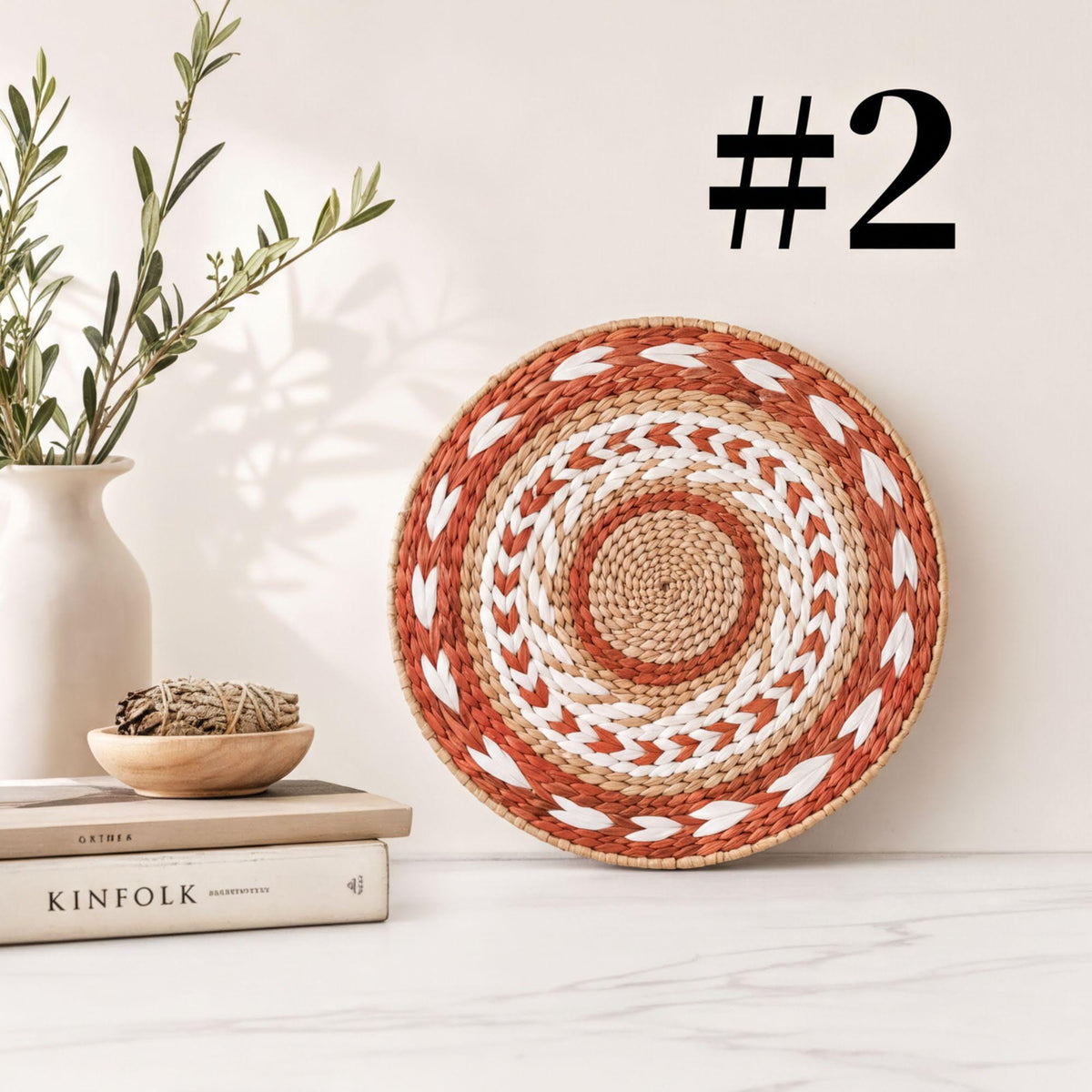 a woven basket with a circular pattern, a stack of books, a white vase with greenery, and a plant on a white marble surface.