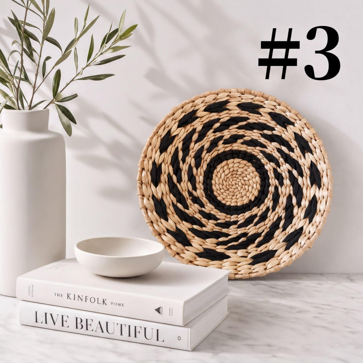 a white vase with a plant, a woven basket, a stack of books, and a bowl on a marble surface.