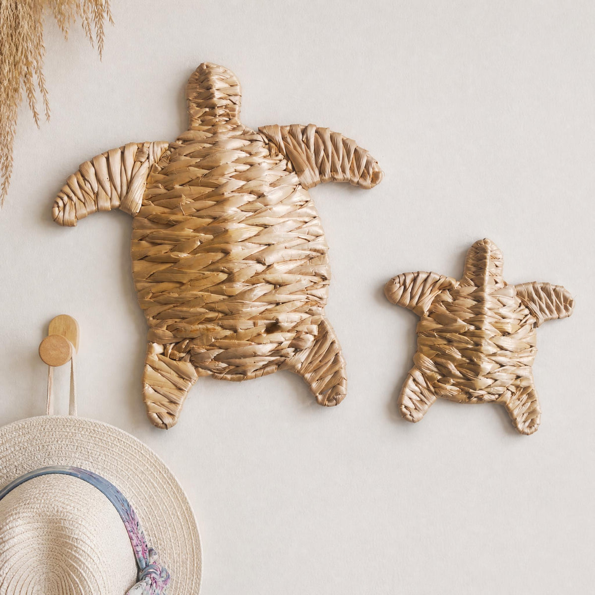 two woven turtle-shaped objects, one larger and one smaller, hanging on a wall.