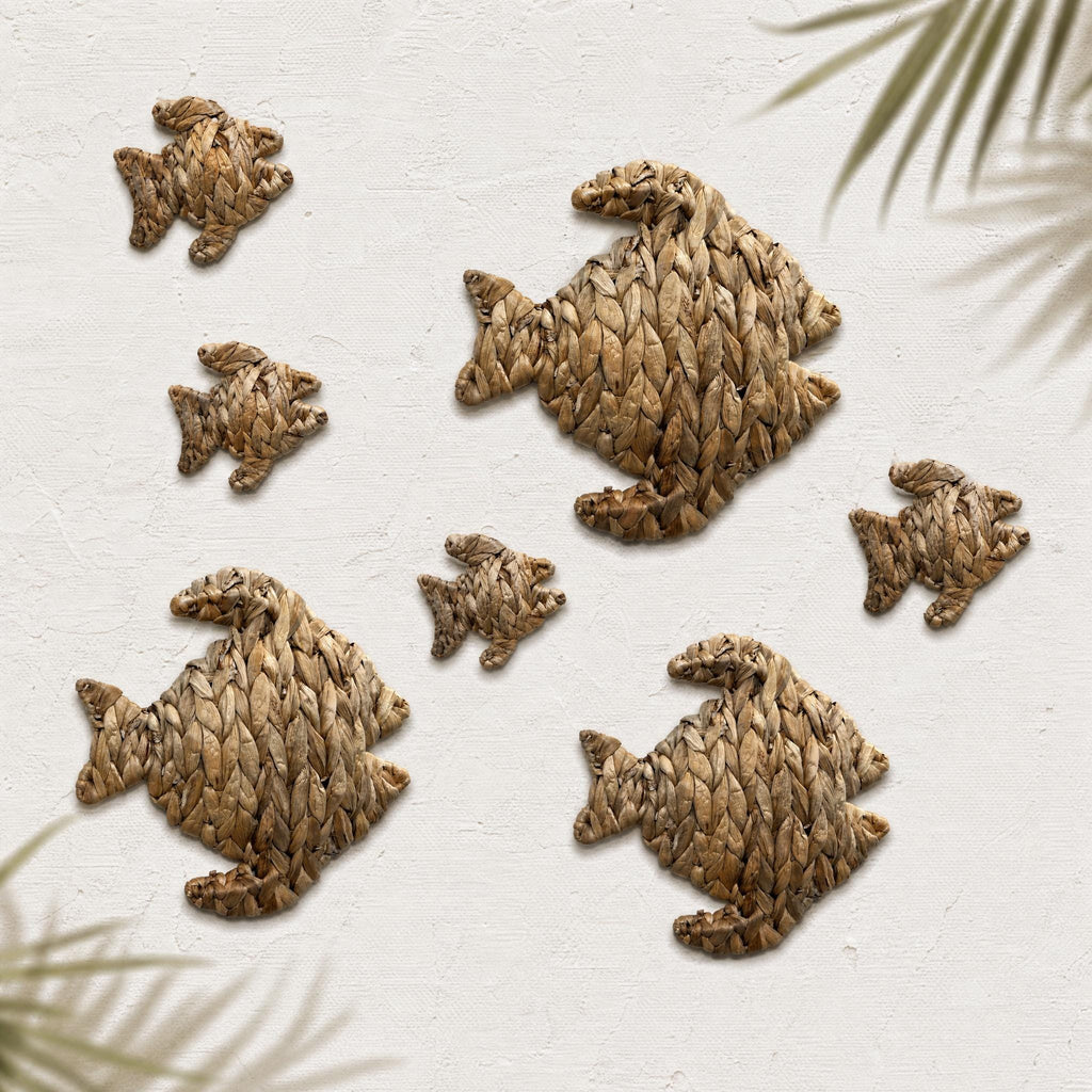 a collection of six fish-shaped objects made of woven materials, arranged on a white background with some green leaves visible in the top right corner.