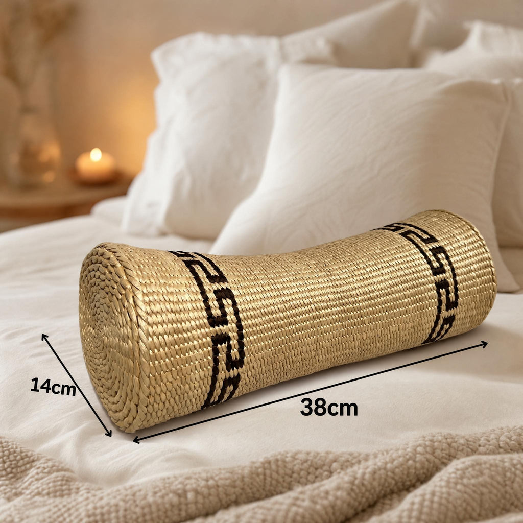 a woven straw pillow resting on a bed, with a candle and white pillows visible in the background.