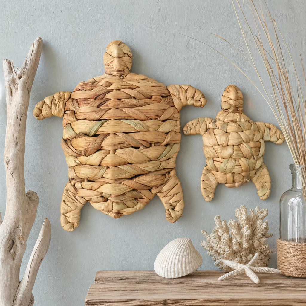 two turtle-shaped wall decorations made of woven materials, placed on a wooden surface. There is also a small vase and some natural elements like a branch and a seashell, creating a coastal or beach-inspired decor.