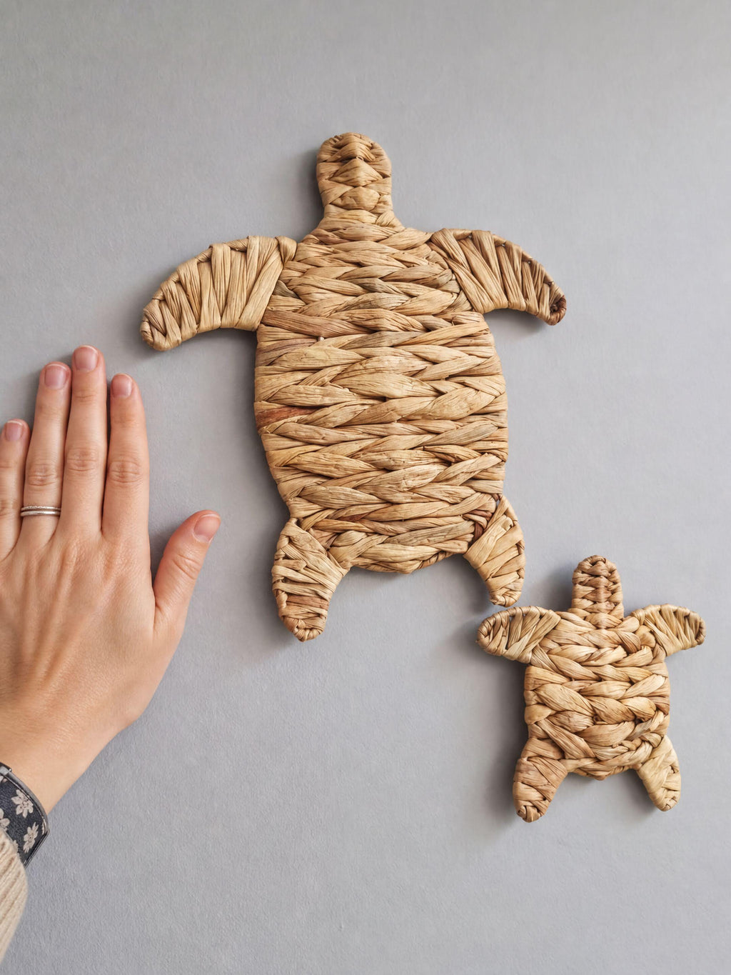 A hand is holding a small woven turtle-shaped object, which appears to be made of straw or similar material.