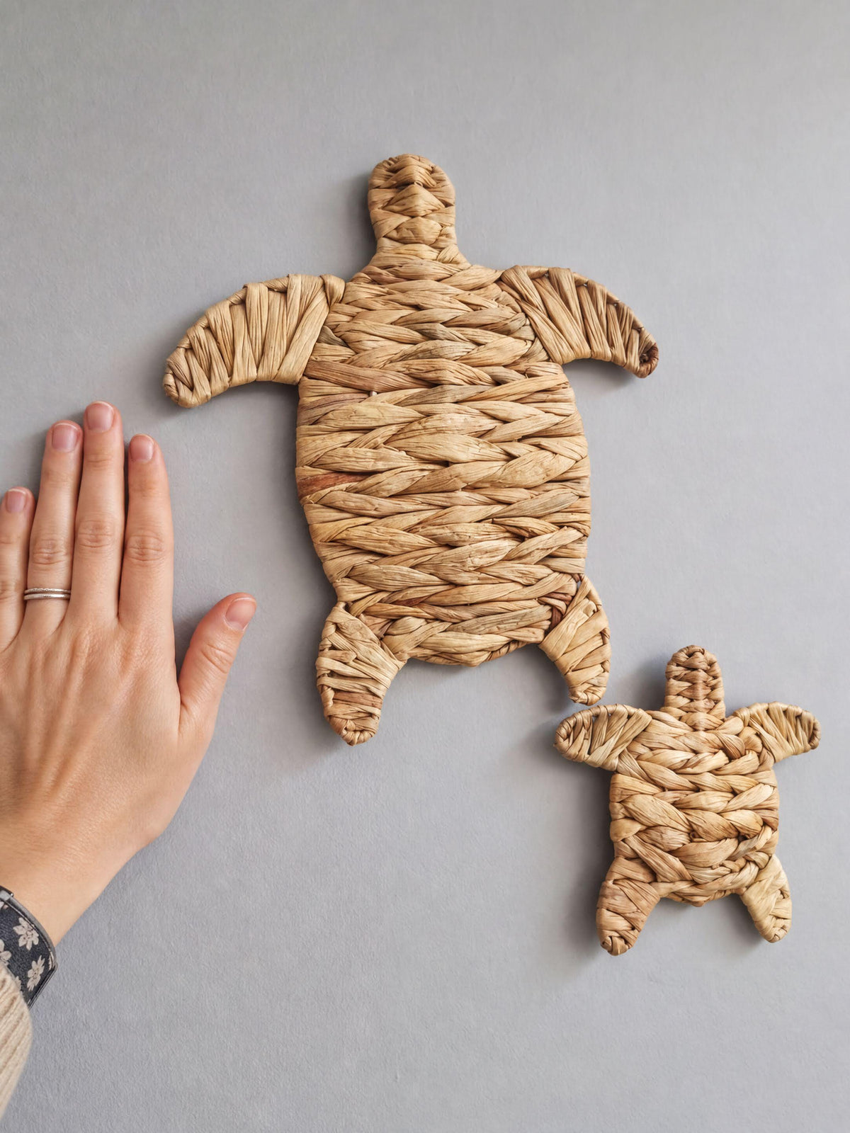A hand is holding a small woven turtle-shaped object, which appears to be made of straw or similar material.