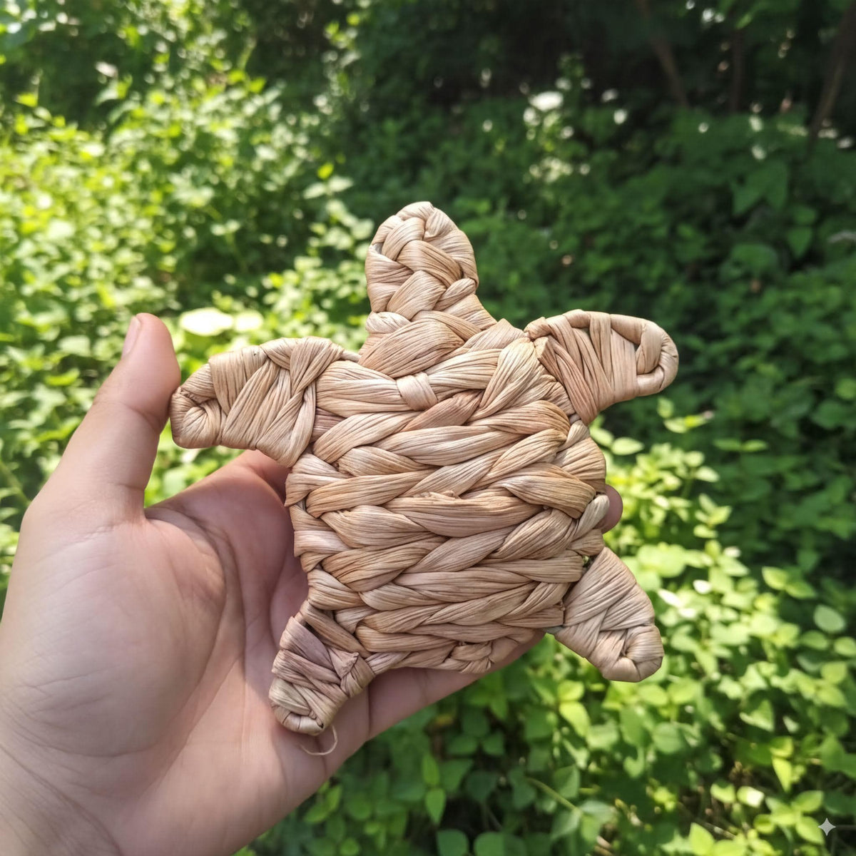A hand holding a woven object resembling a turtle or sea turtle, with a natural, earthy color palette.