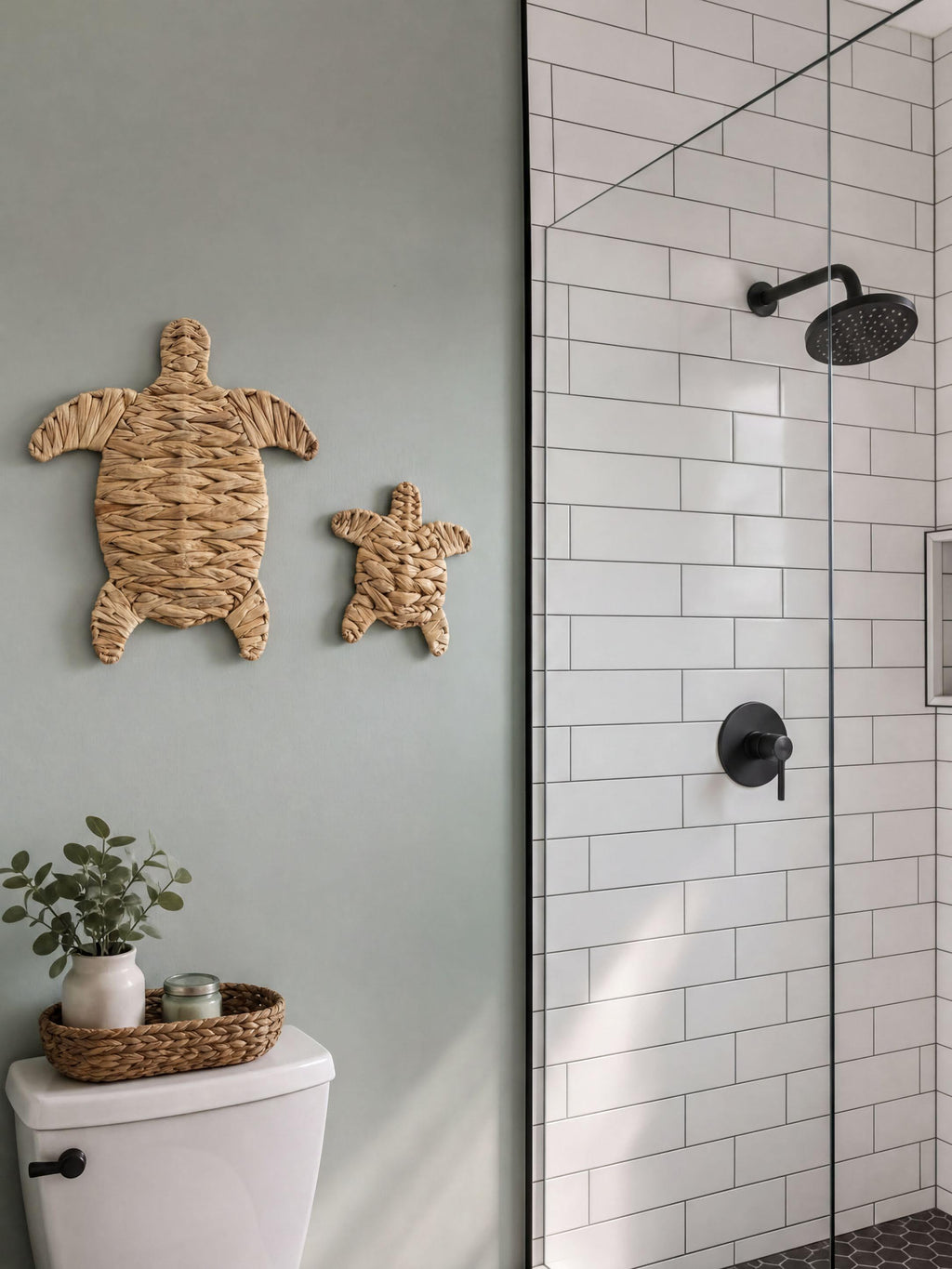 a bathroom with a white tiled wall, a glass shower enclosure, and a small turtle-shaped wall decoration. There is also a small plant on the toilet tank.