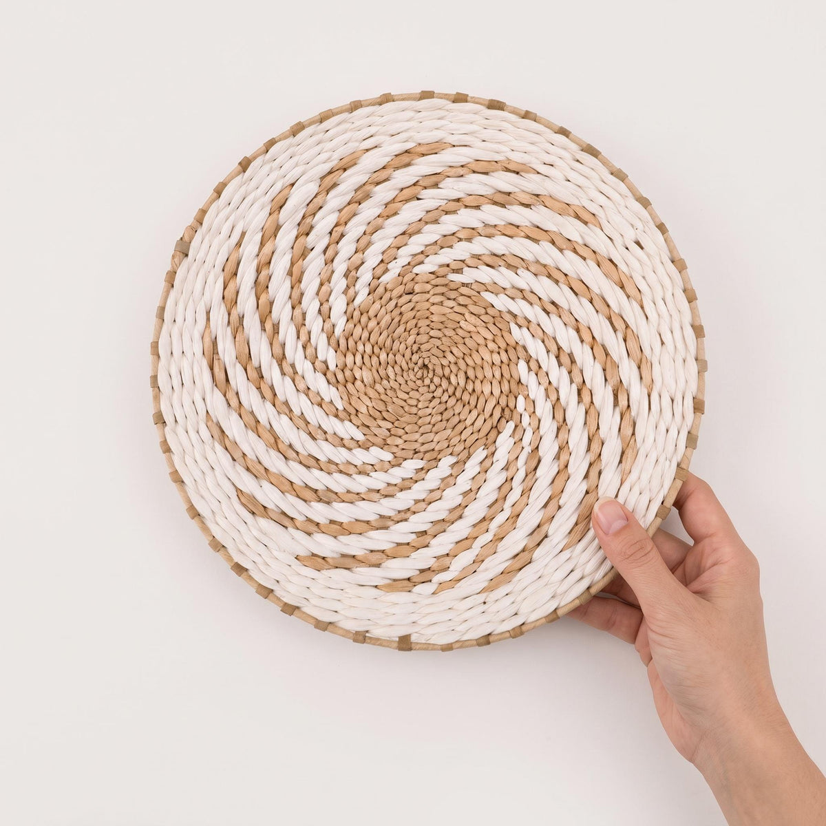 Hand holding the large woven water hyacinth wall basket against a white wall to show its size