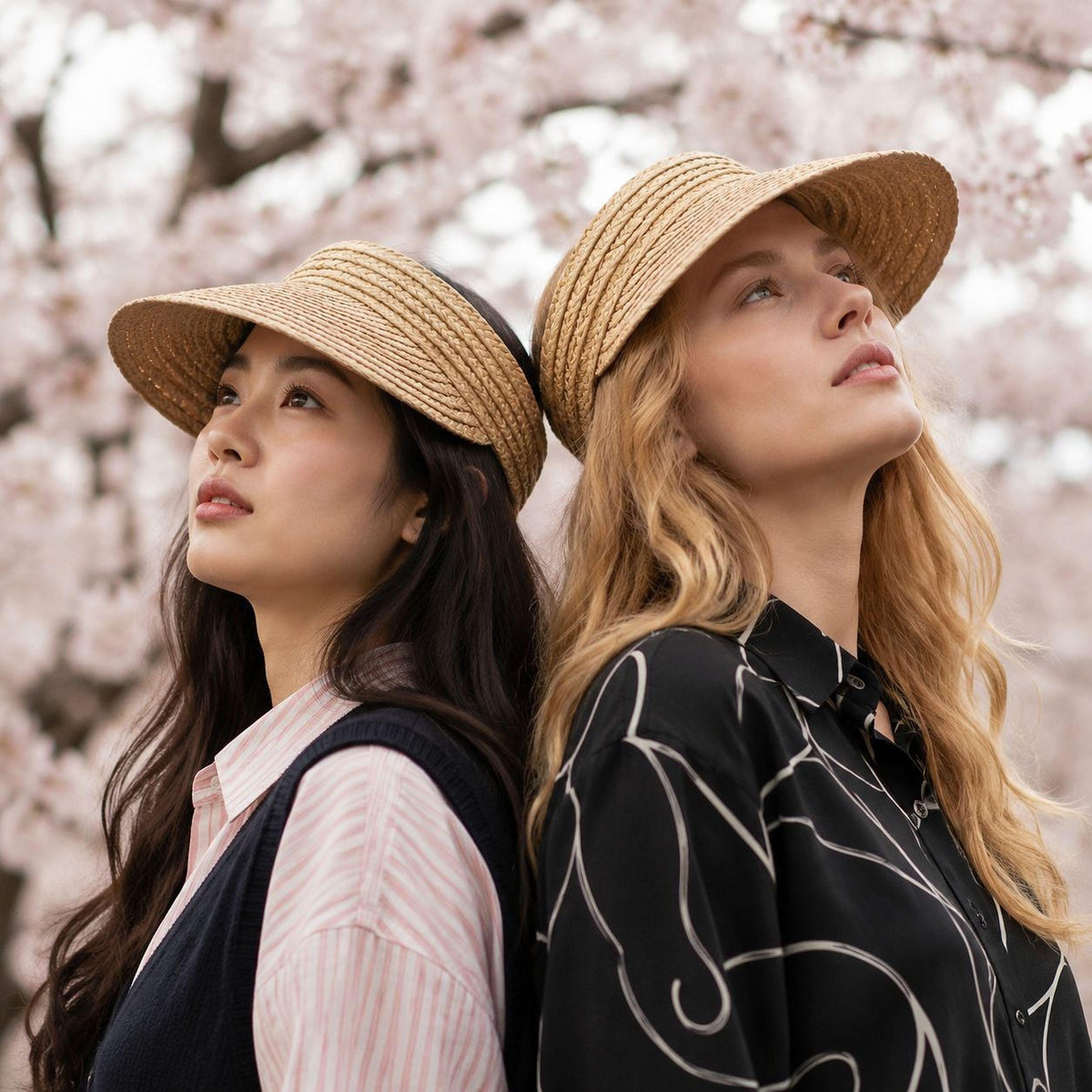 Two women wearing adjustable raffia straw sun visors under cherry blossoms