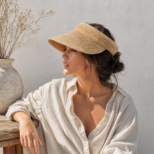 Adjustable raffia straw sun visor with wide brim worn by a woman in a white shirt on a wooden bench