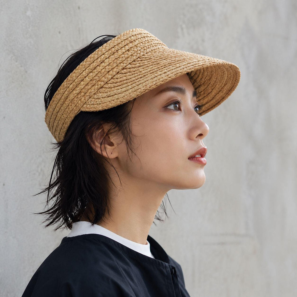 Side view of a woman wearing a wide brim raffia straw sun visor with open top for ponytails
